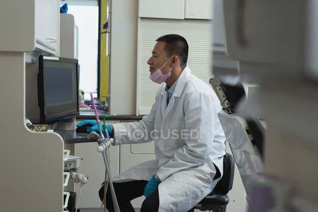 Visão lateral do dentista masculino usando desktop pc na clínica — Fotografia de Stock