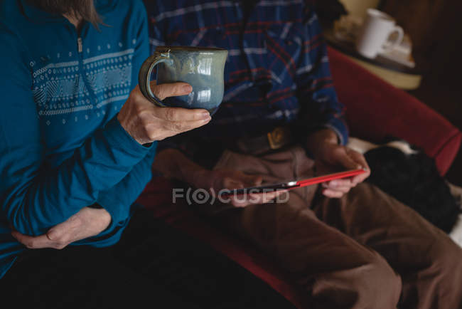 Старша пара використовує цифровий планшет, маючи каву у вітальні вдома — стокове фото