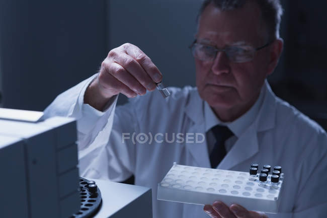 Male scientist placing chemical tube glass bottle on a machine in laboratory — Stock Photo