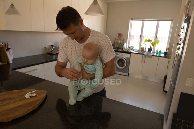 Padre e bambino che tengono la bottiglia di latte in cucina a casa — Foto stock