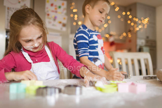 Irmãos cortando biscoitos na cozinha em casa — Fotografia de Stock