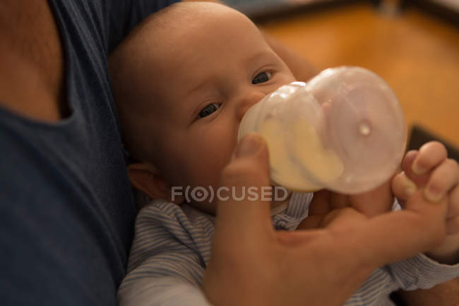 Primer plano del padre alimentando leche a su bebé en casa - foto de stock
