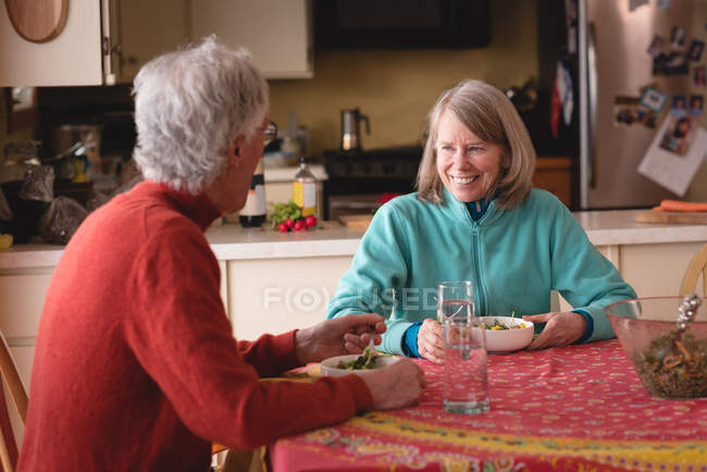 Glückliches Seniorenpaar beim gemeinsamen Essen in der heimischen Küche — Stockfoto