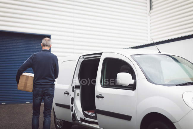 Rear view of delivery man carrying parcel at warehouse — Stock Photo