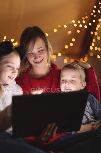 Mãe sorridente e crianças usando tablet digital em casa durante o Natal — Fotografia de Stock