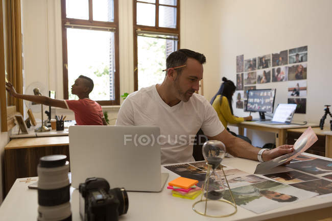 Männliche Führungskraft schaut sich Fotos auf Schreibtisch im Büro an — Stockfoto