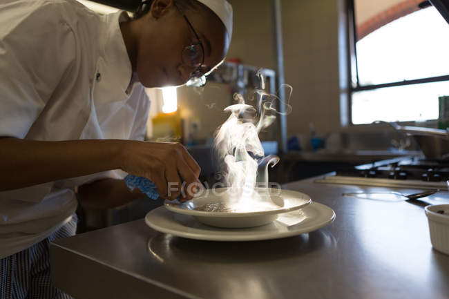Жіночий шеф-кухар прикрашає їжу на тарілці на кухні — стокове фото