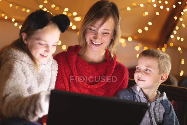 Улыбающаяся мать и дети используют ноутбук дома во время Рождества — стоковое фото