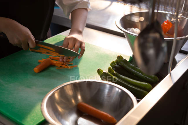 Partie médiane du chef féminin coupant des légumes dans la cuisine au restaurant — Photo de stock
