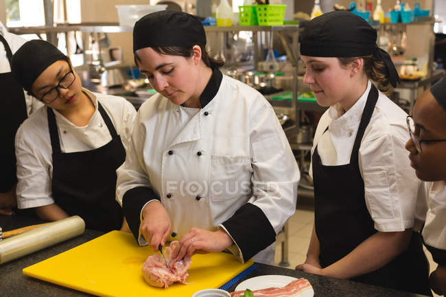 Chef mujer cortando carne en la tabla de cortar en la cocina en el restaurante - foto de stock