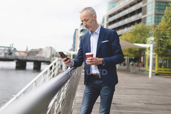 Geschäftsmann an einem sonnigen Tag mit Handy an der Promenade — Stockfoto