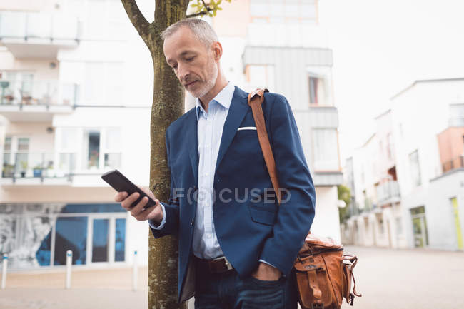 Бизнесмен, использующий мобильный телефон в городе в солнечный день — стоковое фото