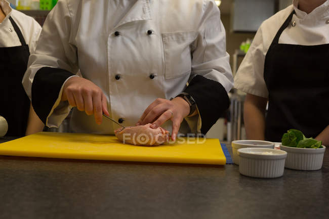 Section du milieu du chef coupant la viande sur la planche à découper dans la cuisine — Photo de stock