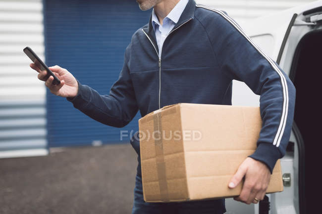 Seção média do homem de entrega usando telefone celular no armazém — Fotografia de Stock