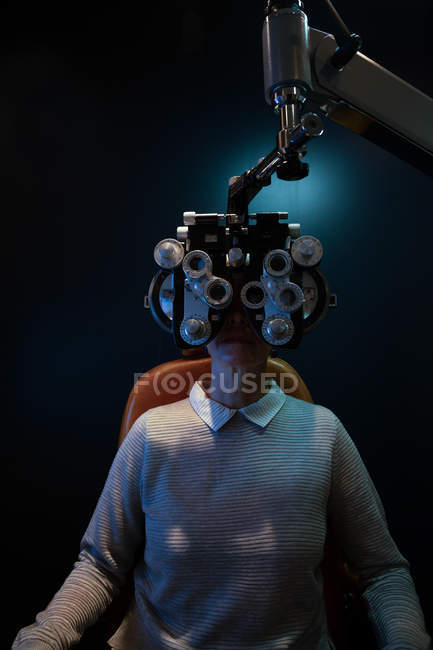 Optometrista examinando los ojos del paciente con foropter en la clínica - foto de stock