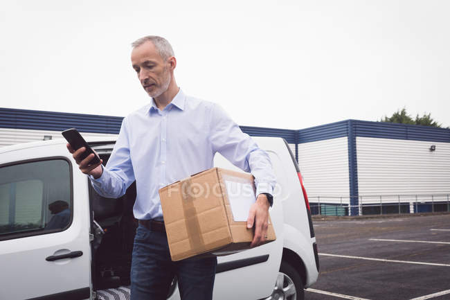 Entrega homem usando móvel no armazém — Fotografia de Stock