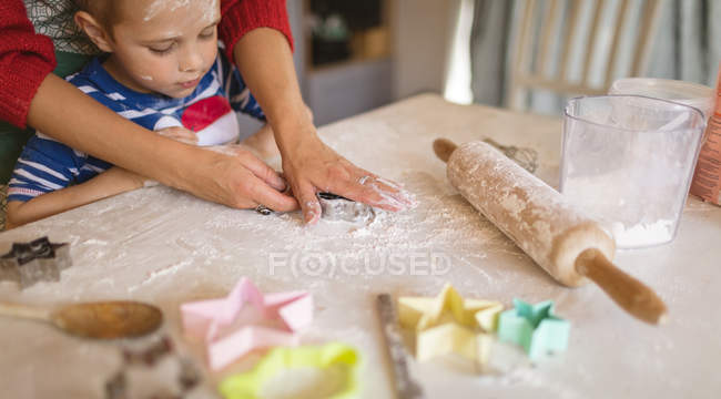 Figlio guardando la madre che taglia i biscotti in cucina — Foto stock