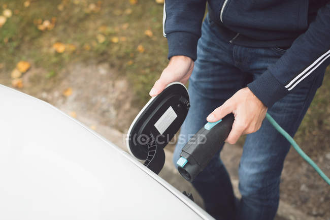 Partie médiane de l'homme rechargeant la voiture électrique à la station de charge — Photo de stock