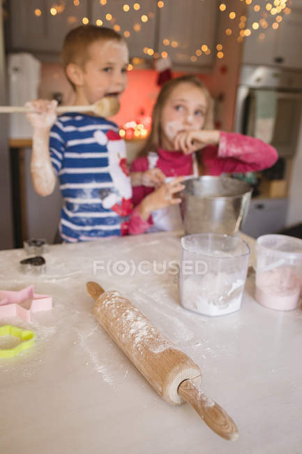 Rolling pin, cookie cutter and siblings tasting the batter in the kitchen — Stock Photo