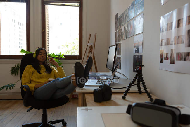 Beautiful female executive listening music in office with legs on table — Stock Photo