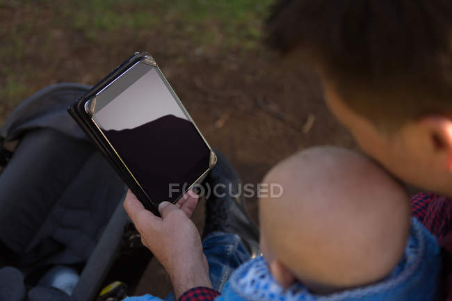 Primer plano del padre y el bebé utilizando la tableta digital en el parque - foto de stock