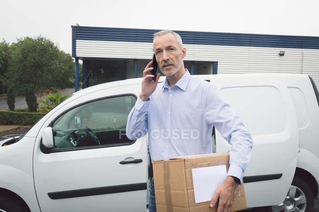 Delivery man talking on mobile phone at warehouse — Stock Photo
