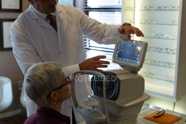 Optometrista che spiega il rapporto visivo sullo schermo dei rifrattori automatici in clinica — Foto stock
