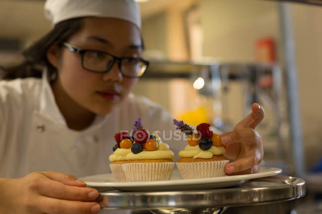 Chef feminino organizando muffins em um prato no restaurante — Fotografia de Stock