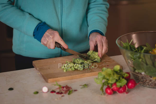 Frau schneidet Brokkoli mit Messer auf Schneidebrett in Küche — Stockfoto