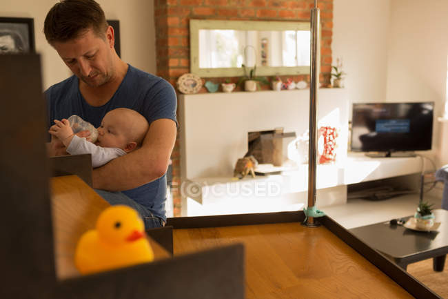 Père donnant du lait à son bébé garçon dans le salon à la maison — Photo de stock