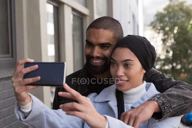 Feliz pareja tomando selfie en la calle de la ciudad - foto de stock