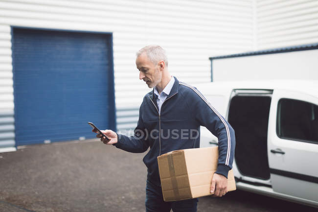 Entrega homem usando telefone celular no armazém — Fotografia de Stock