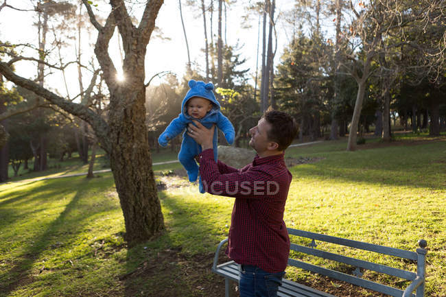 Батько тримає свого малюка в парку в сонячний день — стокове фото