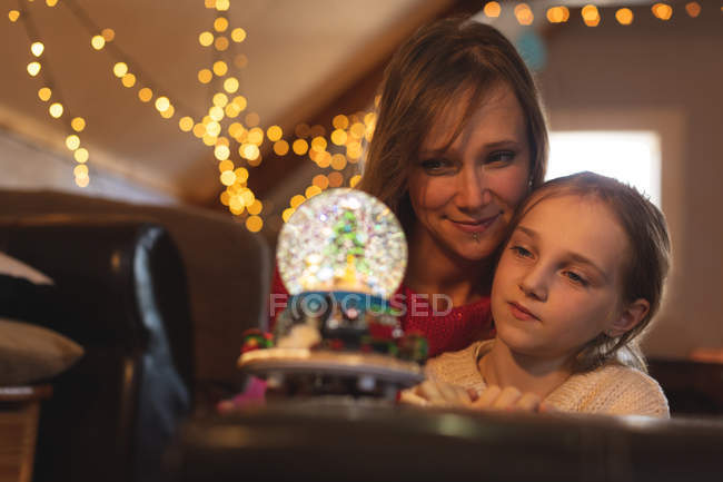 Mother and daughter looking at Christmas tree snow globe at home — Stock Photo