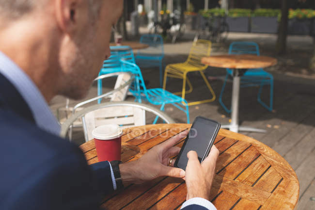 Бизнесмен пользуется мобильным телефоном в кафе на открытом воздухе в солнечный день — стоковое фото