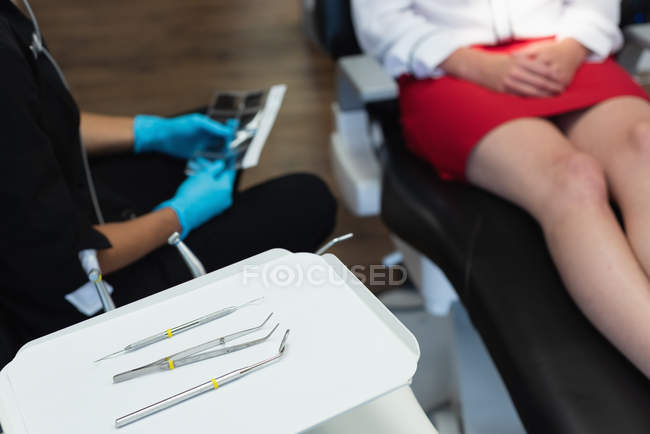 Strumenti dentali in vassoio mentre il dentista femminile interagisce con il paziente in clinica dentale — Foto stock