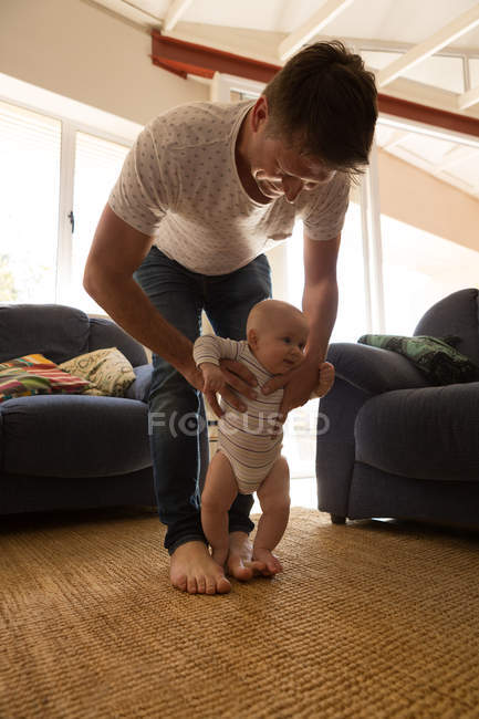 Padre aiutare il suo bambino a camminare in soggiorno a casa — Foto stock