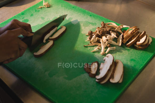 Крупный план повара, режущего грибы на кухне — стоковое фото