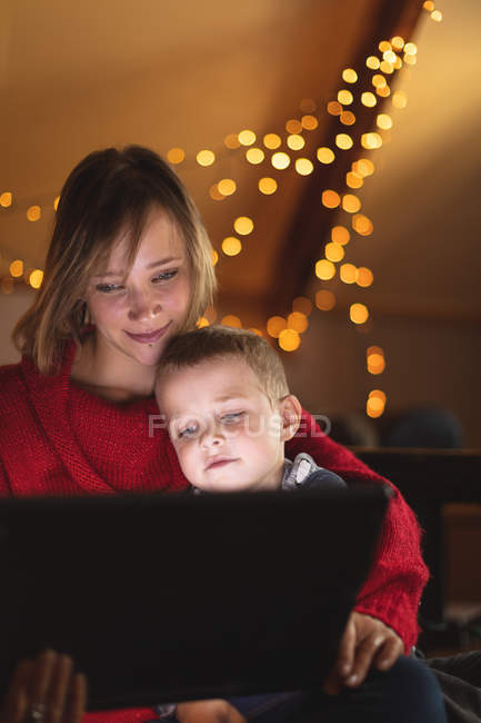 Close-up de mãe e filho usando tablet digital com luzes de Natal no fundo — Fotografia de Stock