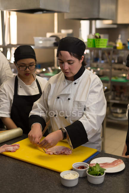 Chef femme coupant de la viande sur planche à découper dans la cuisine au restaurant — Photo de stock