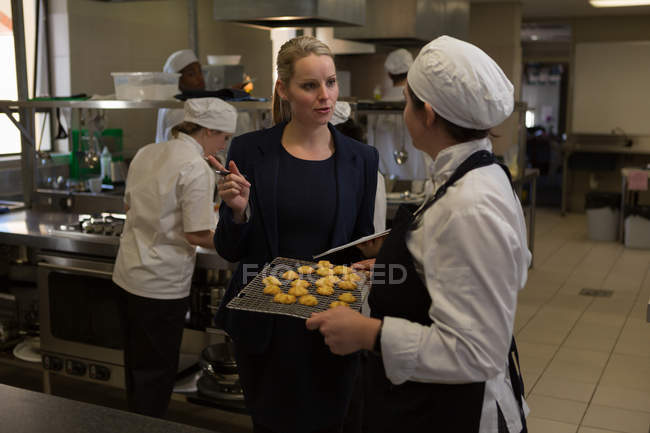 Directora y cocineras que interactúan entre sí en la cocina - foto de stock