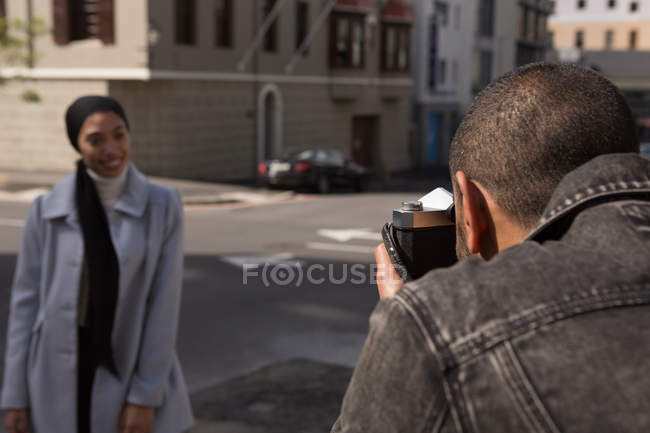 Мужчина фотографирует женщину с цифровым планшетом на городской улице в солнечный день — стоковое фото