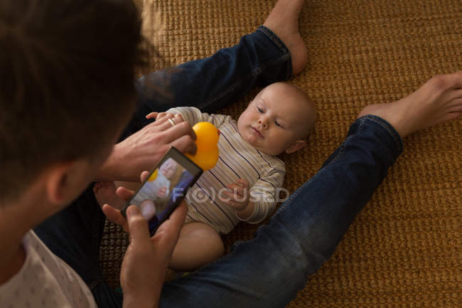 Father clicking photo of his baby boy with mobile phone at home — Stock Photo