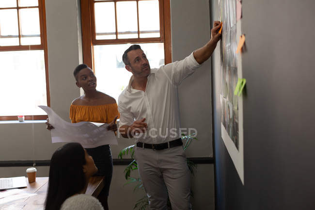Compañeros de negocios discutiendo sobre notas adhesivas en la oficina - foto de stock