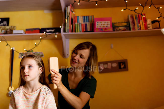Sonriente madre peinando hijas cabello en casa - foto de stock