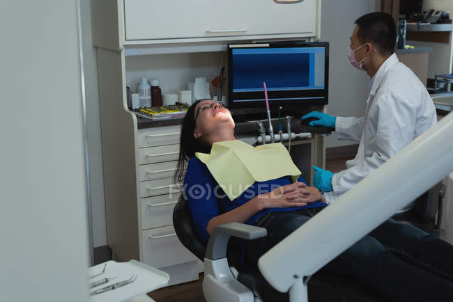 Dentiste masculin utilisant PC de bureau tout en examinant une patiente à la clinique — Photo de stock