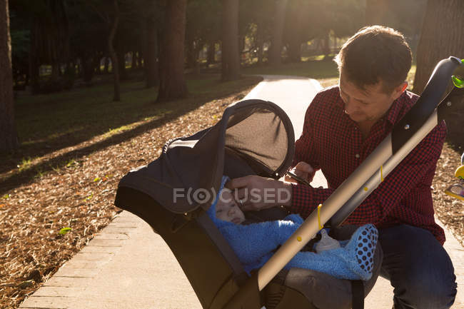Батько зі своїм маленьким хлопчиком у колясці в парку в сонячний день — стокове фото
