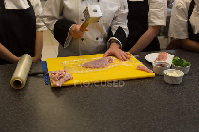 Средняя часть шеф-повара с помощью мясного молотка на кухне — стоковое фото
