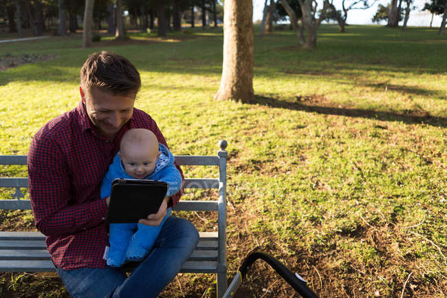 Pai e menino usando tablet digital no parque em um dia ensolarado — Fotografia de Stock