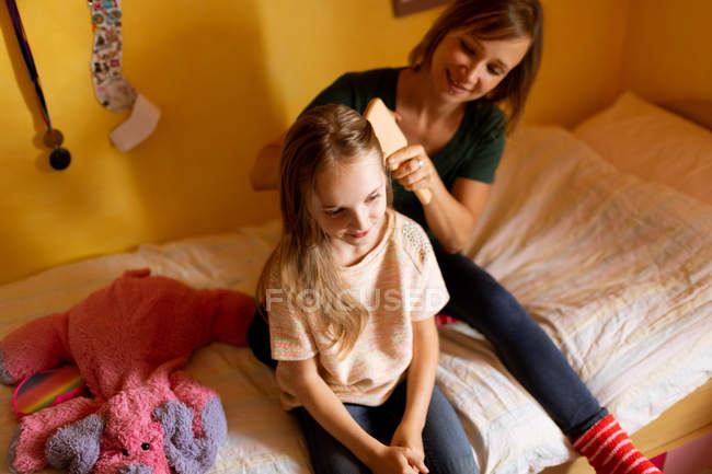 Mère souriante peigner les cheveux des filles à la maison — Photo de stock